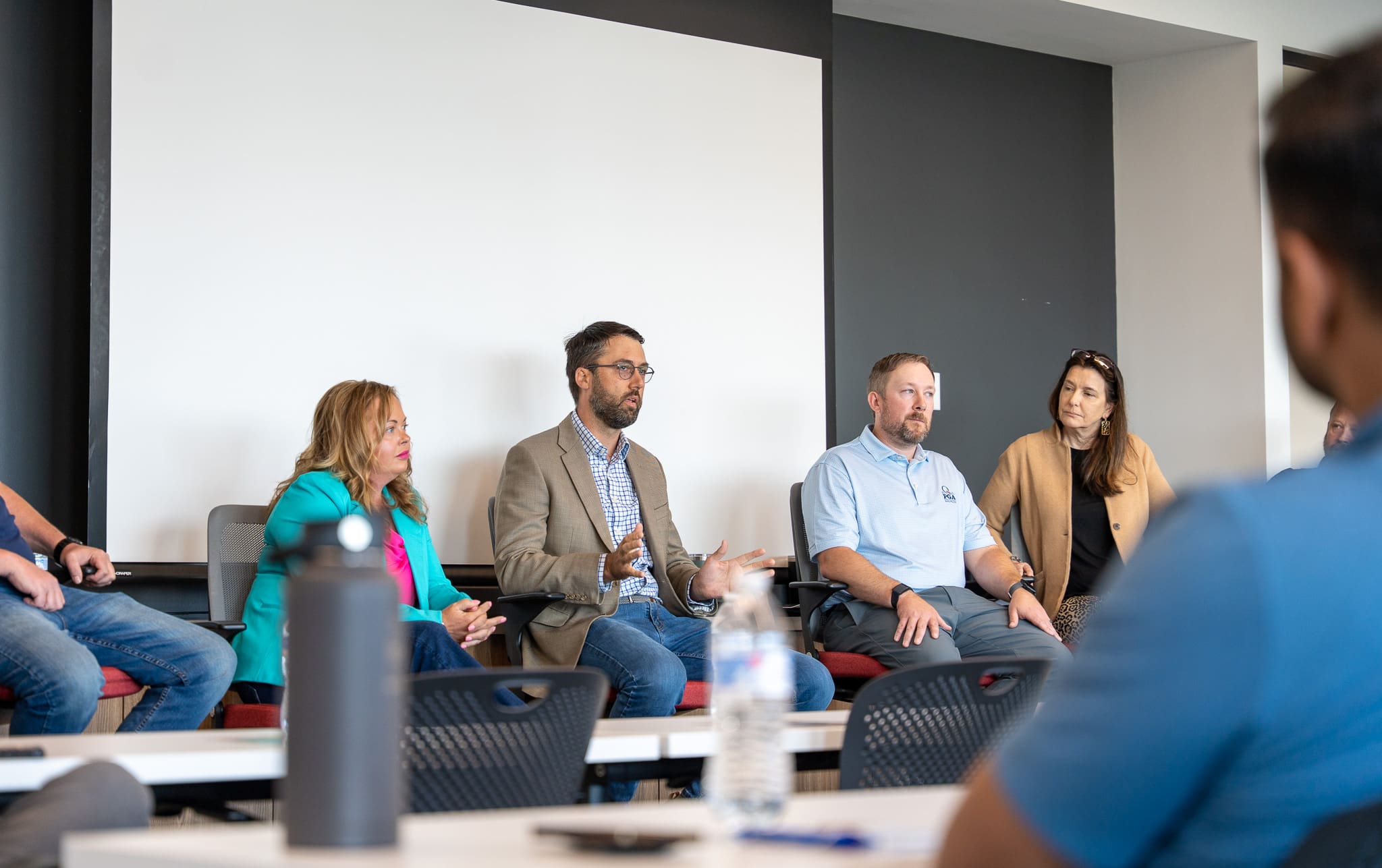 Panelists speak on stage at the 2025 Women at Work event hosted by Samet Corporation, with a seated audience listening attentively in a modern conference space.