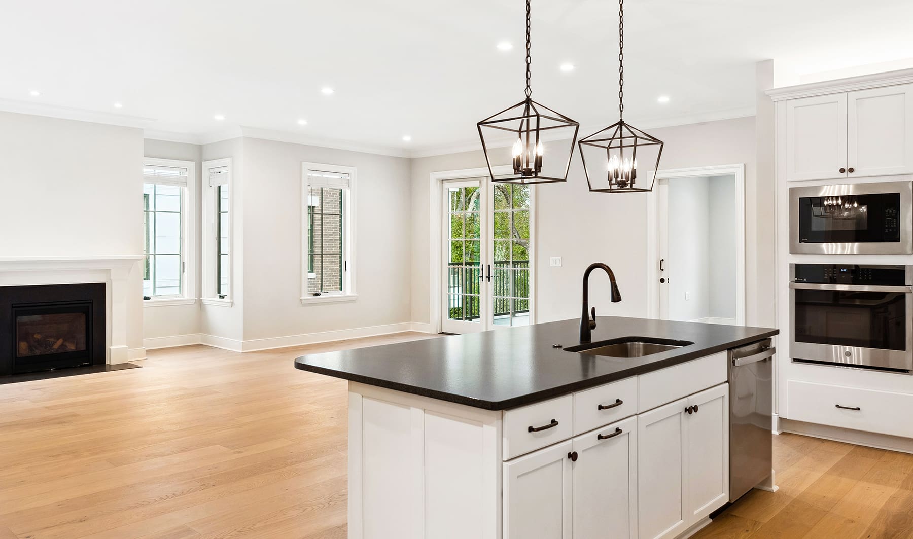 Modern white kitchen with dark countertops, island, pendant lights, and open floor plan